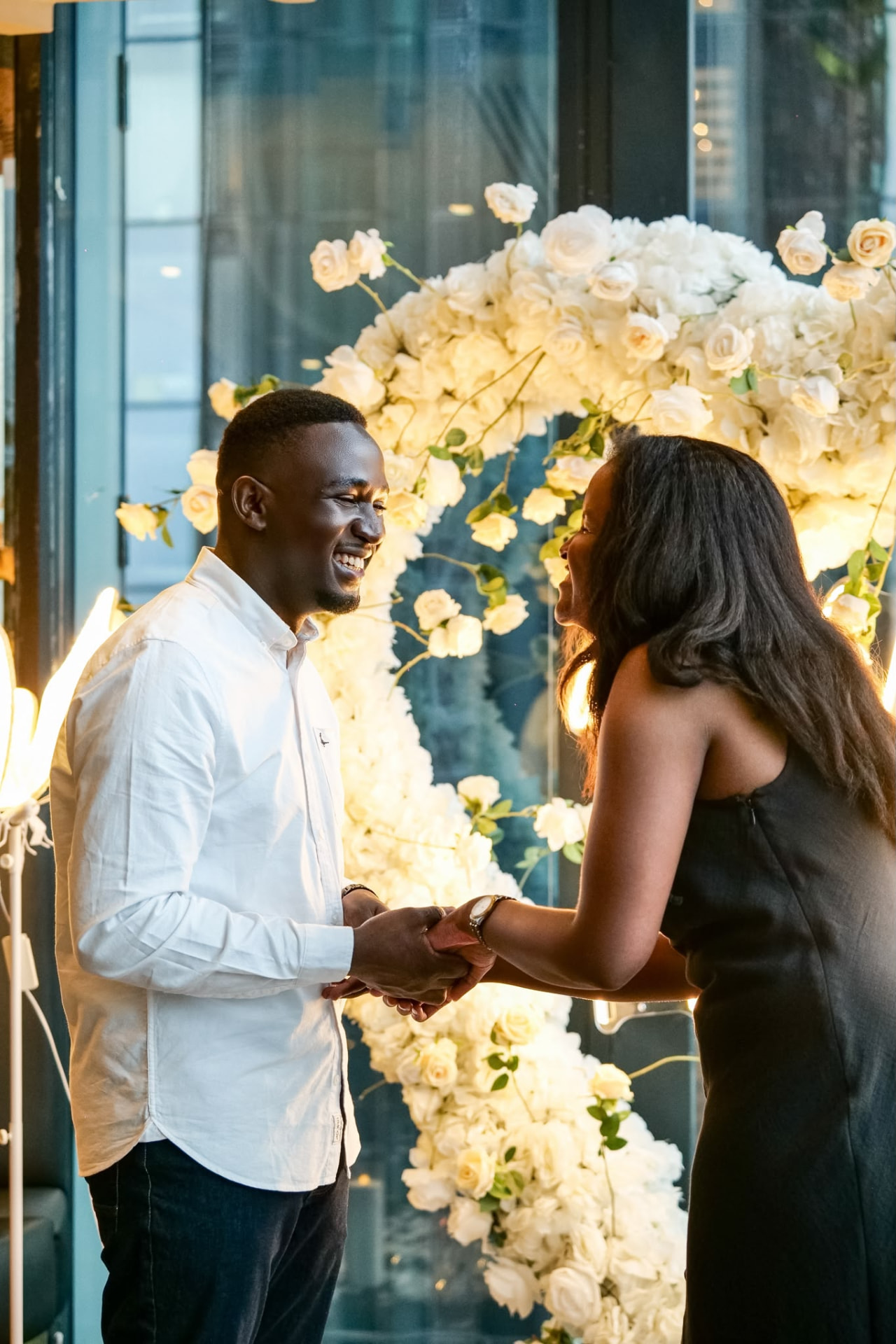 Emmanuel and Martha holding hands before a white floral arch